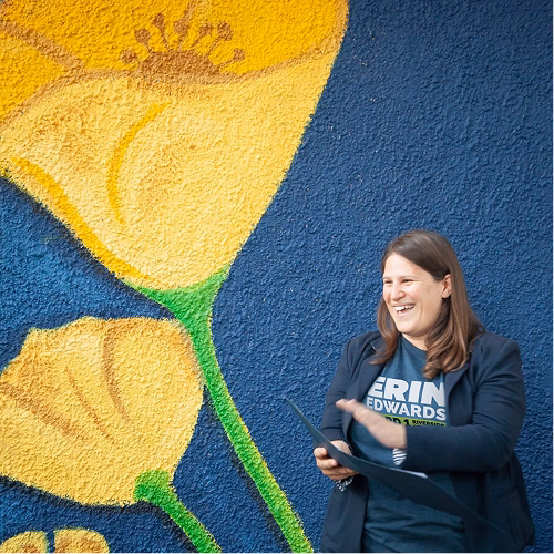 A large mural of the Erin Edwards poppy logo painted on a wall, with Erin standing beside it